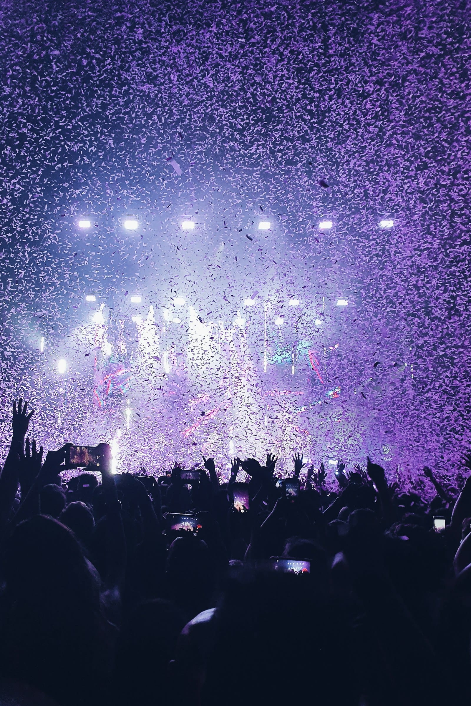 A crowd at a concert with purple confetti falling under bright stage lights