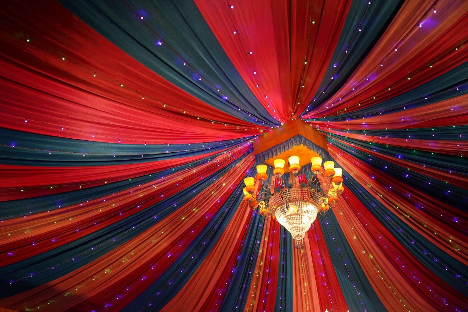 A crystal chandelier hanging from a ceiling draped in colorful red and blue fabric