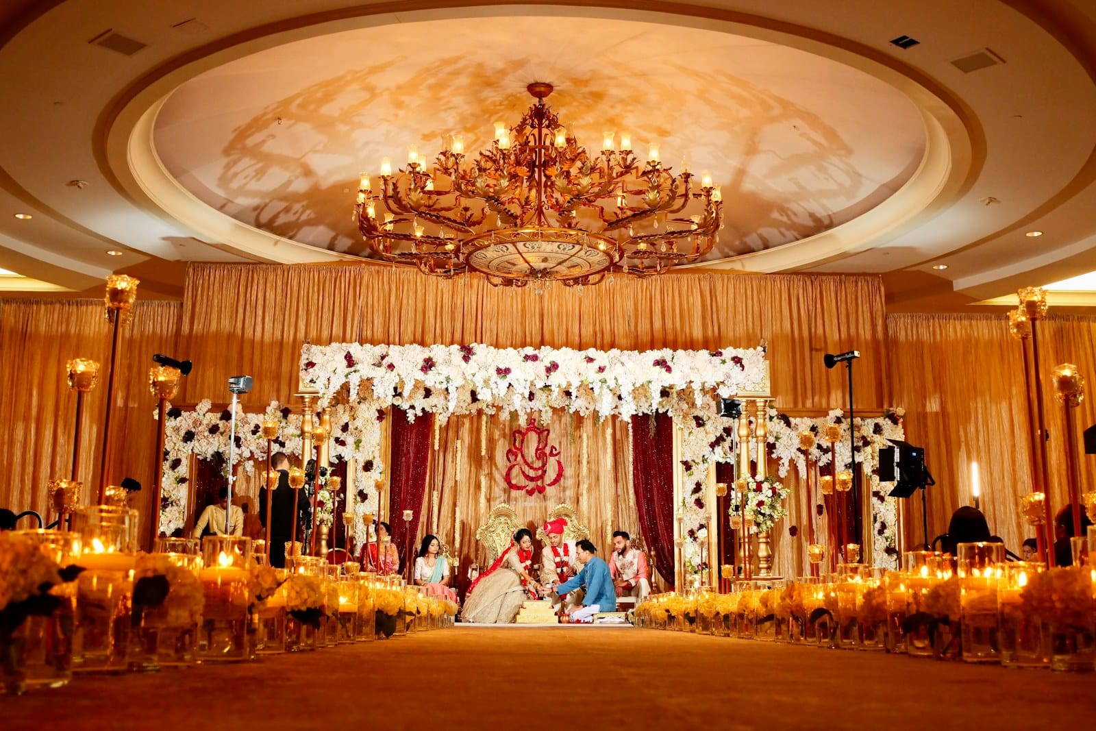 A couple performing a wedding ritual under a floral canopy in a ballroom